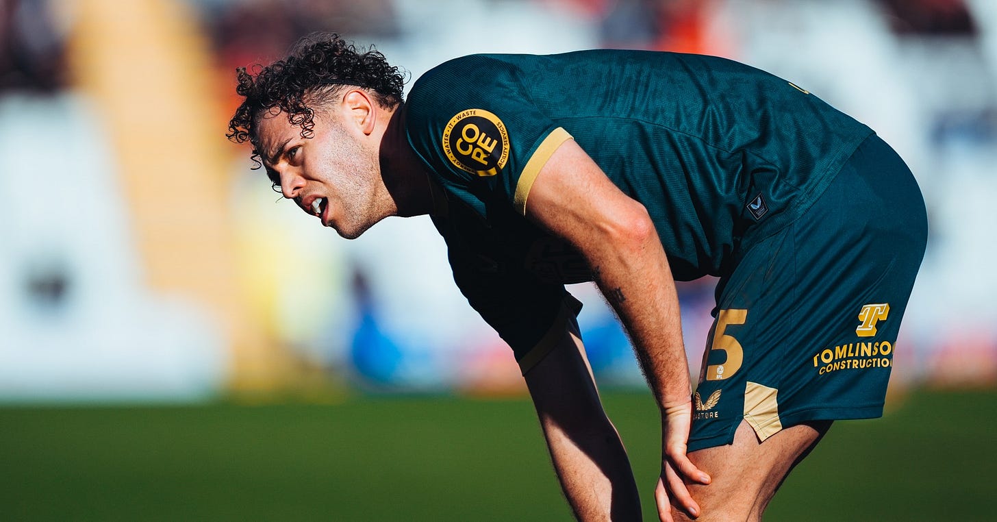 Huddersfield Town player Jake Charles, wearing the club’s green third kit, leans over, with the pitch in the background.