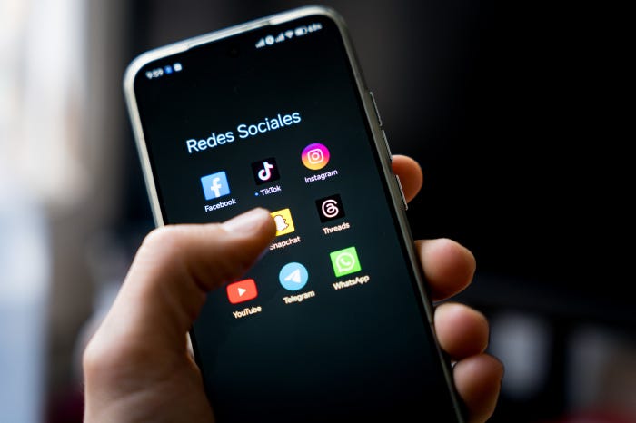 A hand holds a smartphone showing social-media app icons. A hand holds a smartphone showing social-media app icons.