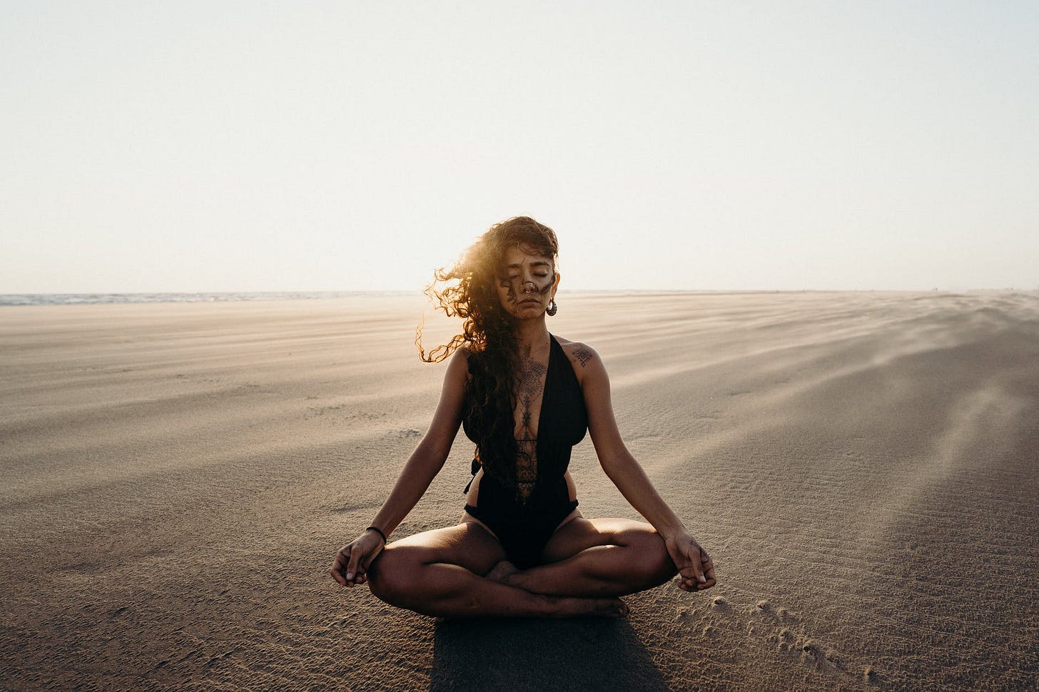 woman in black tank top and blue denim jeans sitting on brown sand