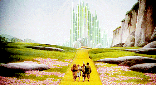 gif of alice in wonderland scene with alice, toto, and her friends happily skipping along the yellow brick road towards emerald city.