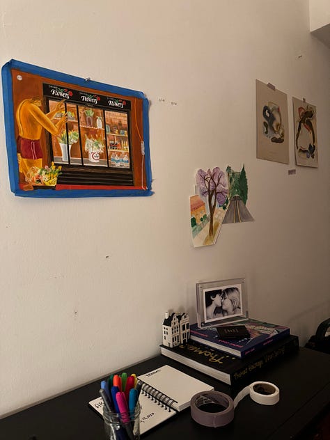 Photo 1: People gathering in a living room with vaulted ceilings. Photo 2: A painting and 3 drawings hung on a wall. Photo 3: A surrealist painting of amorphous creatures hanging from a tree. Photo 4: People gathered around the surrealist painting. Photo 5: A collage with cartoon images of a trail to the ocean and a butterfly, and bold text reading: traces of a path, losing sight of the sea. Photo 6: People and a red dog gathered around a man playing guitar. Photo 7: Ink and pastel drawings of two circles meeting. Photo 8: a pile of shoes at a door. Photo 9: Silhouettes of people through tall windows from outside at night.