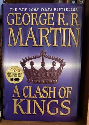 A Clash of Kings by George R. R. Martin book cover. Purple background with a brown crown.
