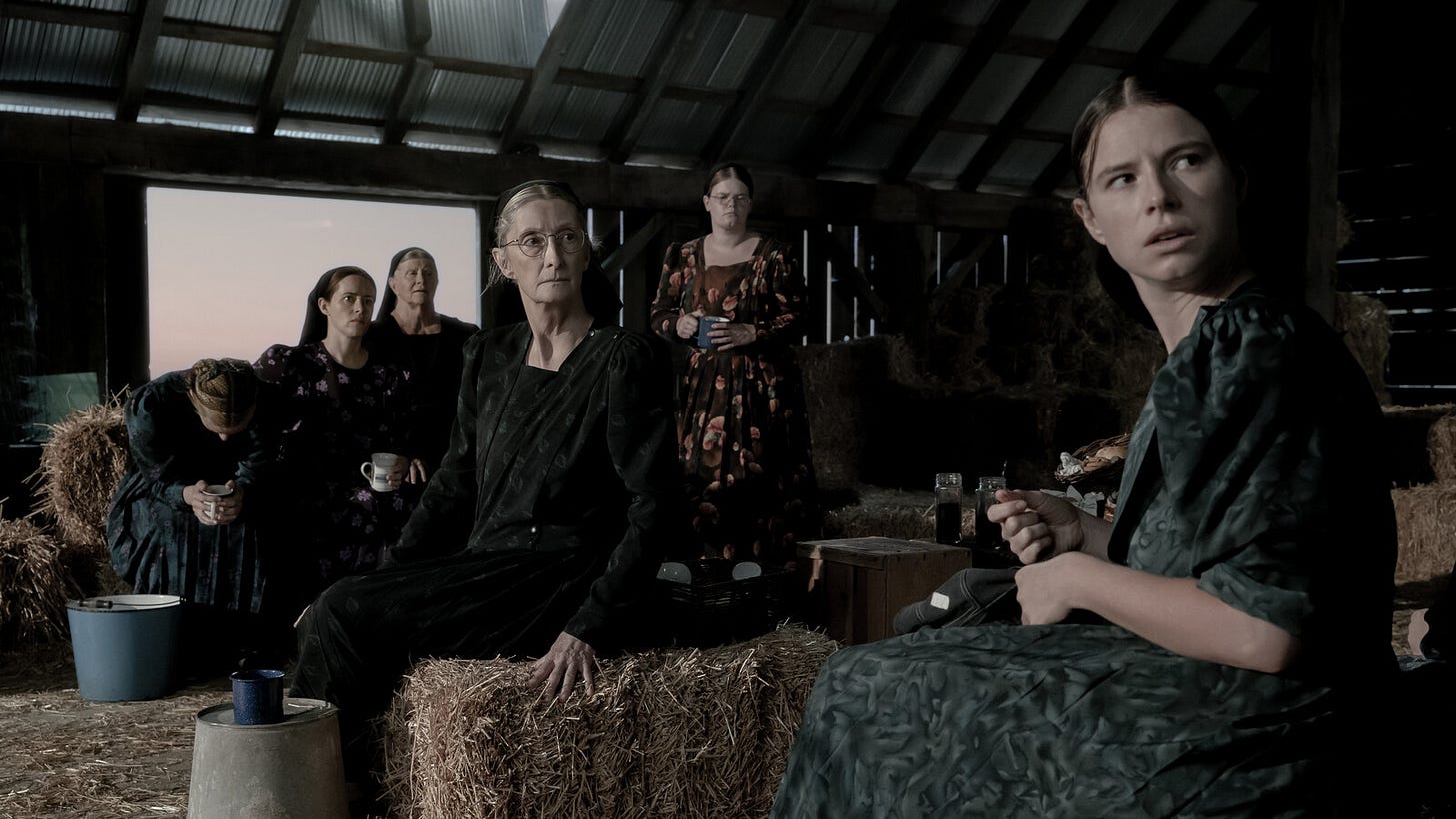 A still from the movie Women Talking, showing a gathering of conservatively-dressed women gathered in a barn