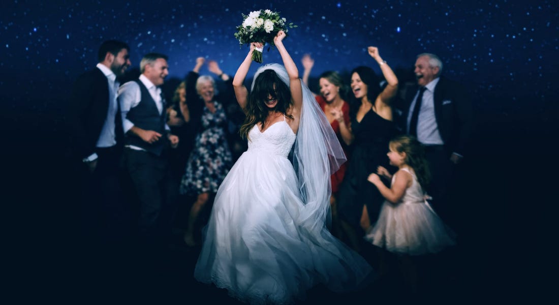 A group of people standing in front of a starry sky partying, with a bride in the middle with a bouquet in the air A group of people standing in front of a starry sky partying, with a bride in the middle with a bouquet in the air