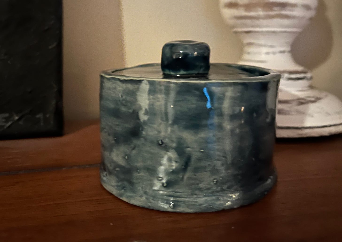 Photo of a handmade little jar glazed a denim blue color sitting on a wood mantel.