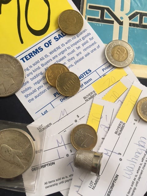 A collection of yellow and white auction tickets, a variety of coins, a silver thimble and a blue and white decal with the letters B and M to form a railroad track.
