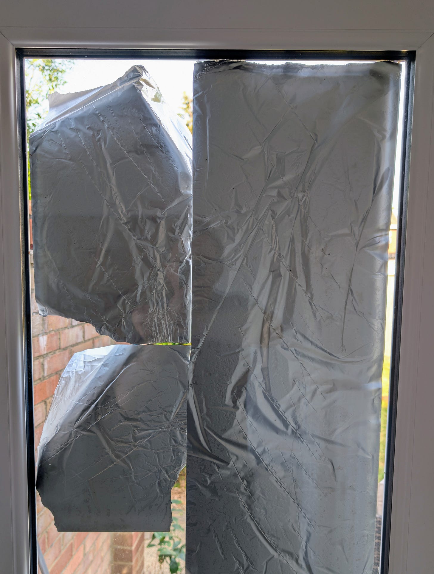 Looking out the backdoor window, the view is blocked by exterior tinfoil that is coming loose. 