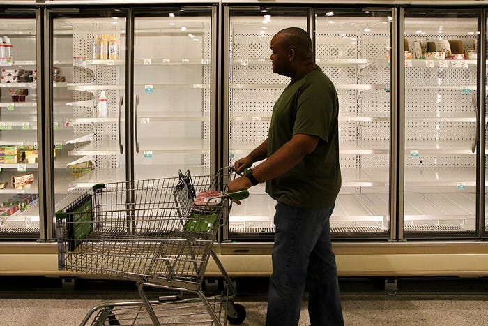 A Black man walking through empty food aisles with an empty cart.
