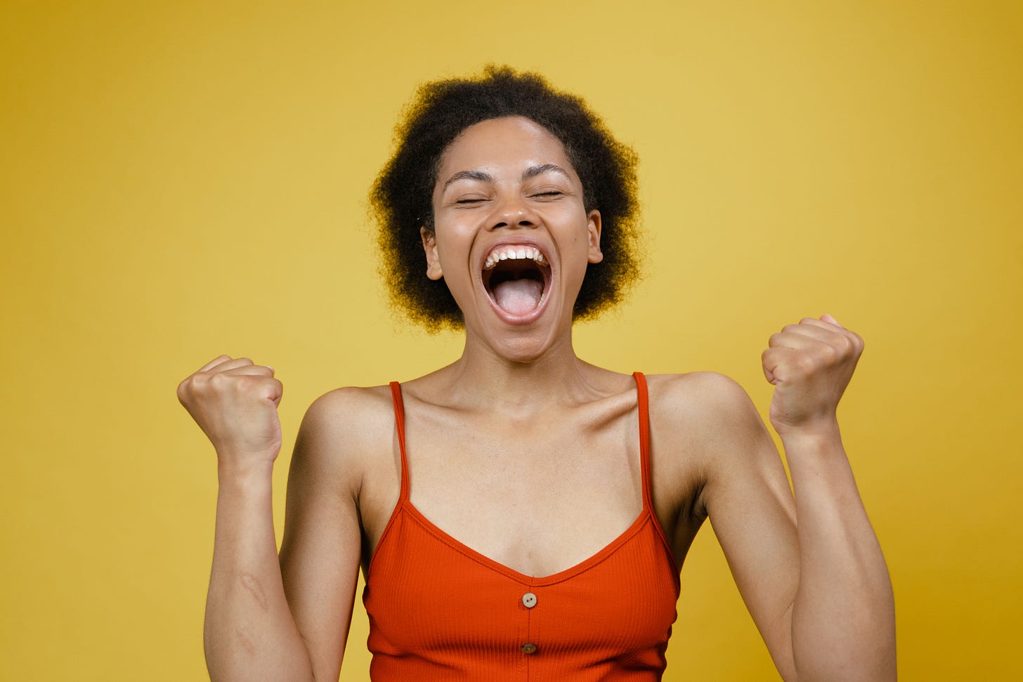 A young woman who is happy, ecstatic, thrilled, exuberant, deli rious, head thrown back, shouting with overwhelming happiness, fists pumping in waves of joy