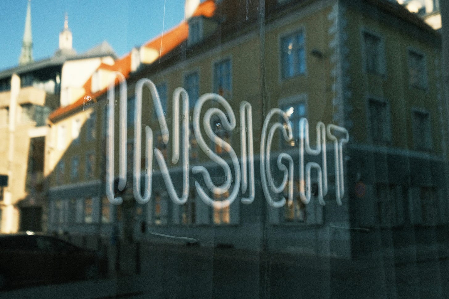 Photo of a white neon sign of the word ‘insight’ in a window that is reflecting the yellow building with a red roof which is opposite the window. Photo of a white neon sign of the word ‘insight’ in a window that is reflecting the yellow building with a red roof which is opposite the window.