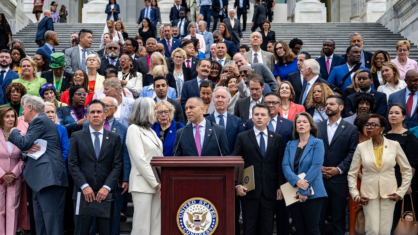 A group of House Democrats gathers on the U.S. Capitol steps, with Leader Hakeem Jeffries speaking at a podium.