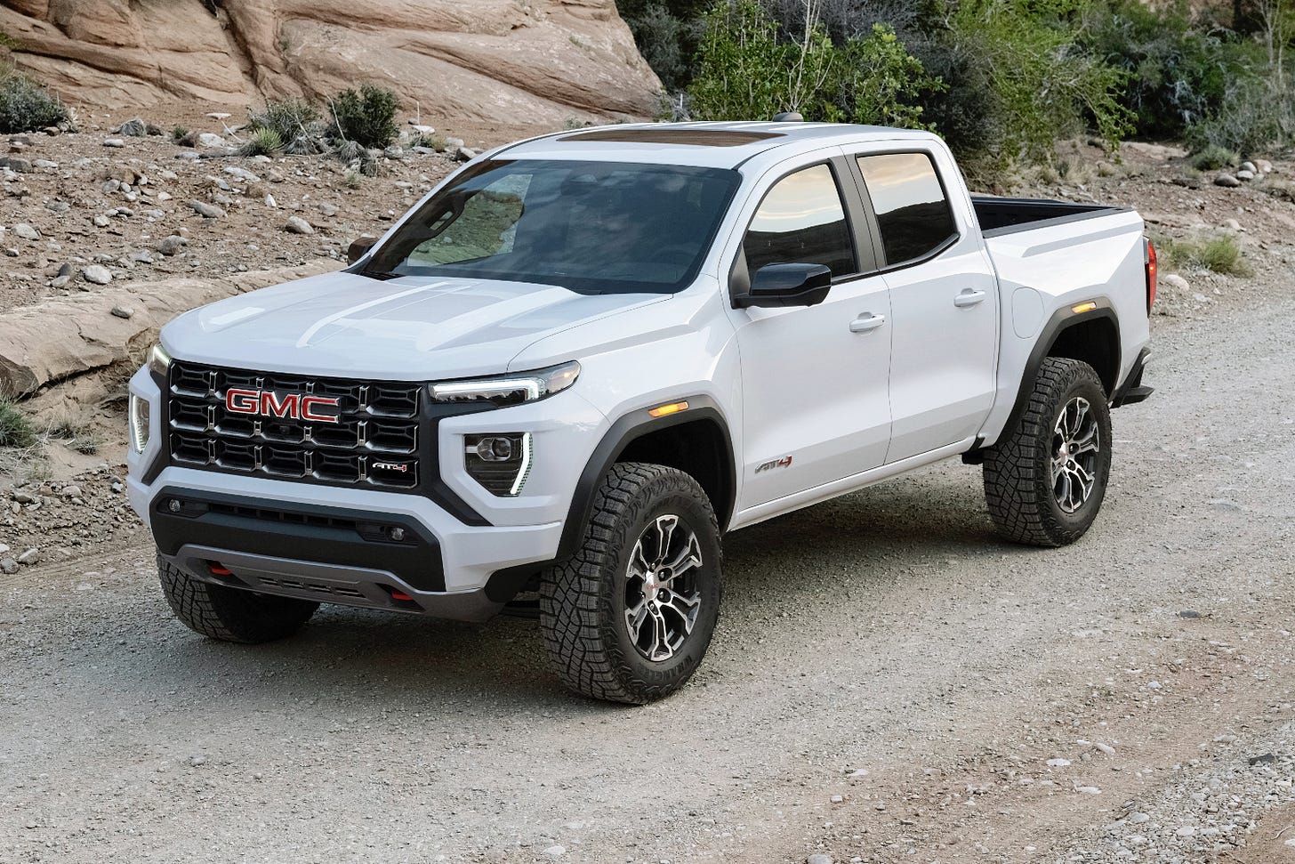 A white 2023 GMC Canyon AT4 is parked on a trail near some rocks.