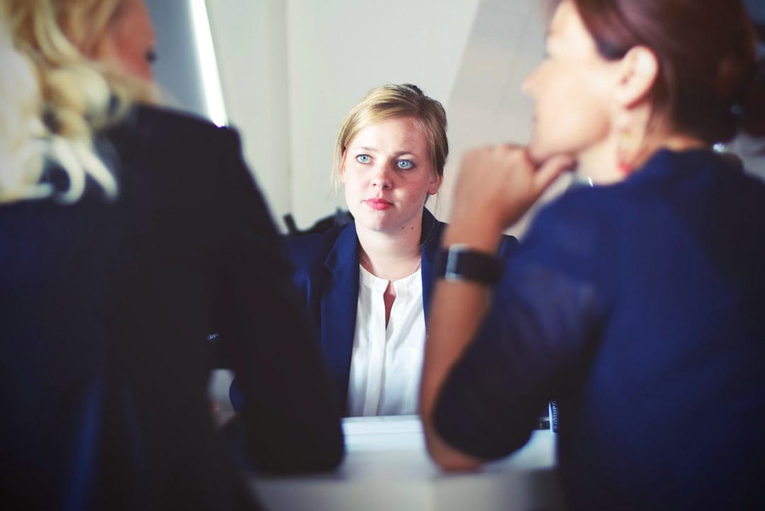 Professional woman in business attire engaged in conversation during an interview, photographed from across the table showing focused attention and authentic interaction Professional woman in business attire engaged in conversation during an interview, photographed from across the table showing focused attention and authentic interaction
