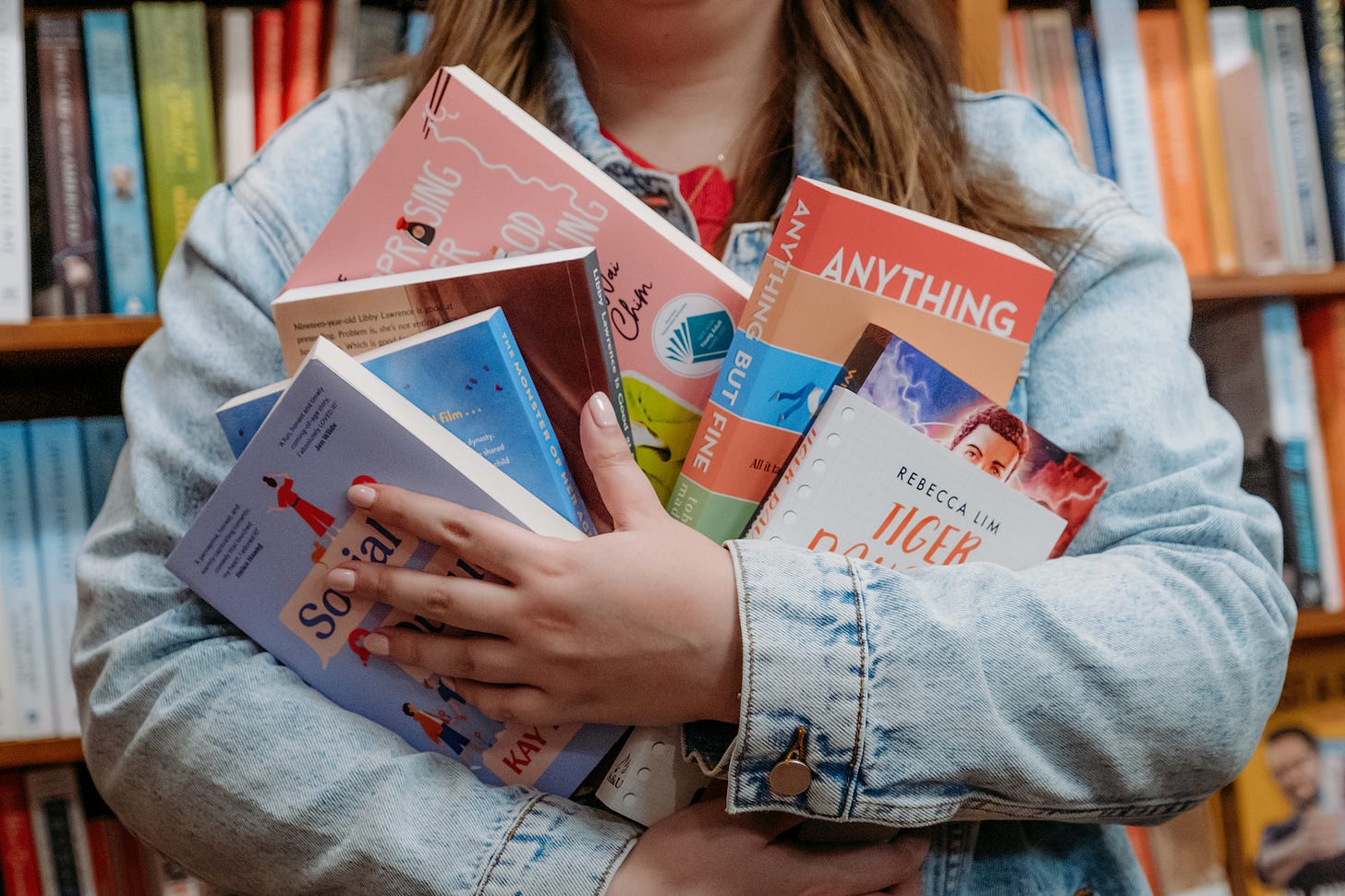 Julia stands in front of a bookcase holding a giant handful of her favourite YA novels. You can only see the novels, not Julia's face.