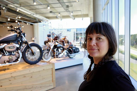 Barber Vintage Motorsports Museum Sign; vintage motorcycles on display; Jessica with her hair in two braids in one of the areas of the bike museum;dozens of bikes stacked on a very tall display; King Kenny Roberts wearing a cowboy hat and sitting on a yellow bike
