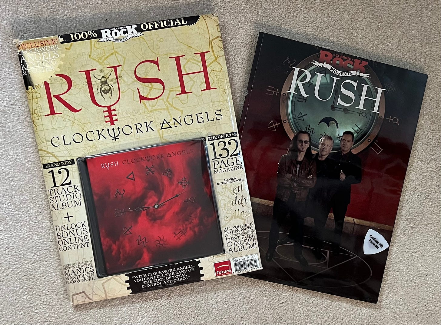 Two special editions magazines and a CD from Classic Rock magazine that are dedicated to Rush's Clockwork Angels album. A white Critical Hit Parader guitar pick is tastefully positioned on top of one of the magazines.