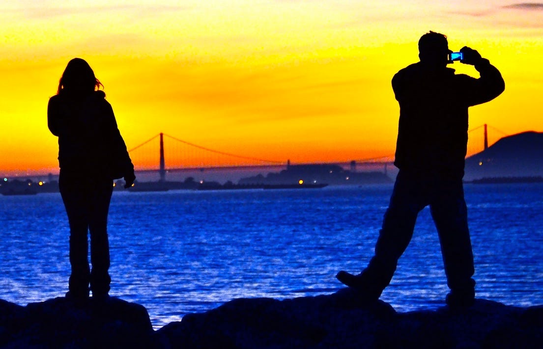 A silhouette of a couple of people standing on rocks by water

Description automatically generated
