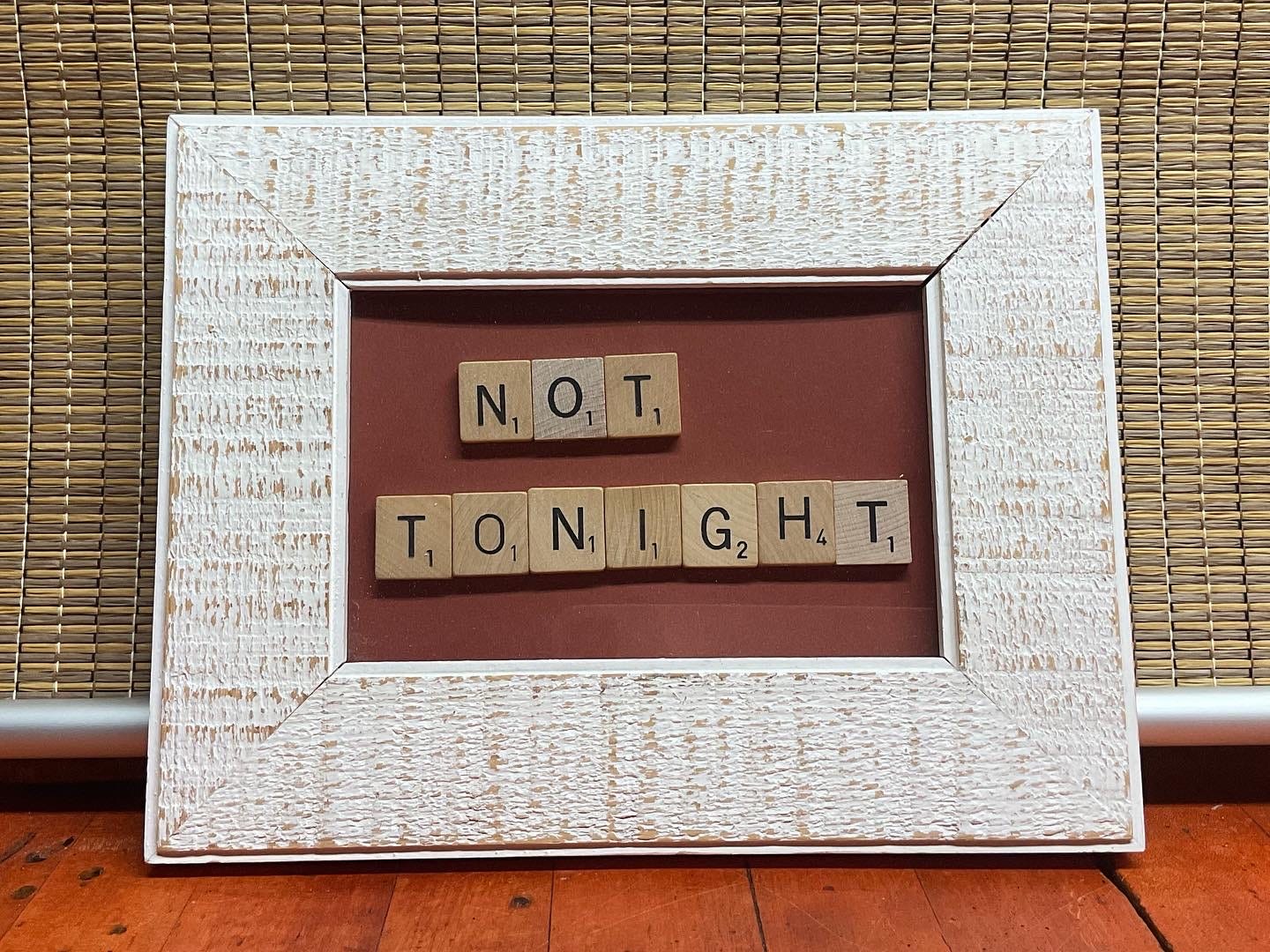 White picture frame with scrabble tiles spelling out the words "Not Tonight". 