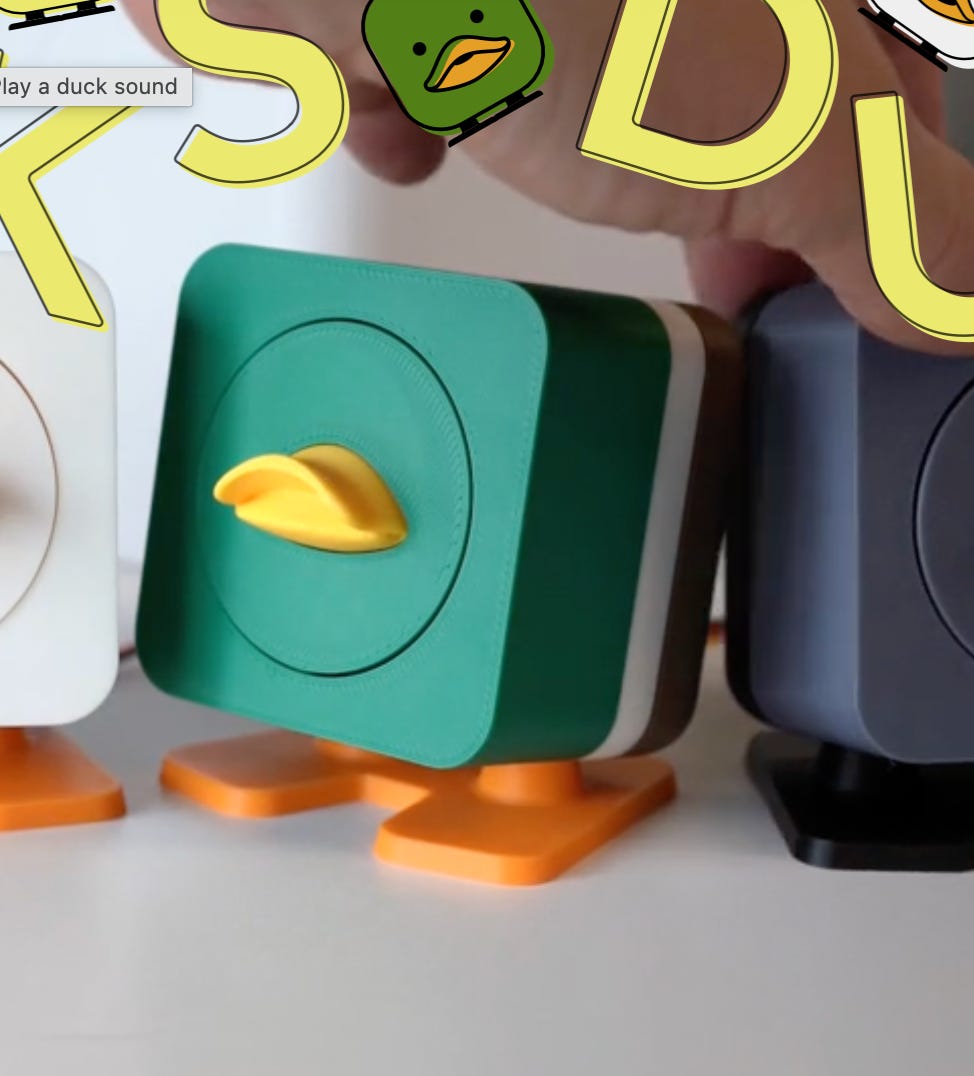 Row of colorful 3D-printed duck-shaped gadgets with orange feet and yellow beaks; the green one in front is being touched, with the tooltip "Play a duck sound."