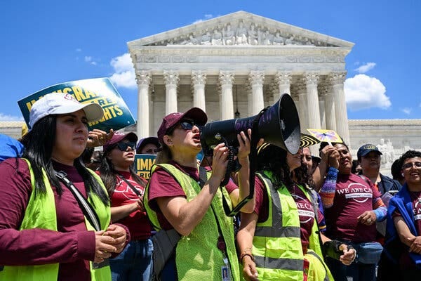 A group of demonstrators, including a person with a megaphone, protest outside the Supreme Court