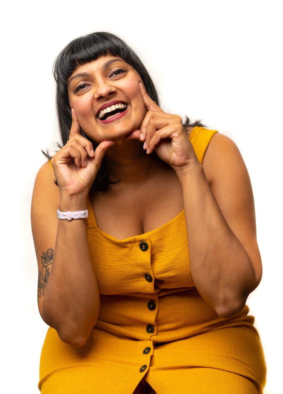 Nisha is in a mustard yellow dress and is smiling while framing her face in a silly way