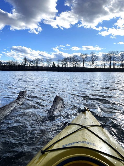 Feet in sandals resting on edge of kayak, pants rolled up. Photo of front of yellow kayak in river. Feet resting on windowsill in fleece socks, pants rolled down.