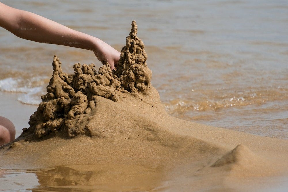 Un castillo de arena en una playa con una persona que lo alcanza Un castillo de arena en una playa con una persona que lo alcanza
