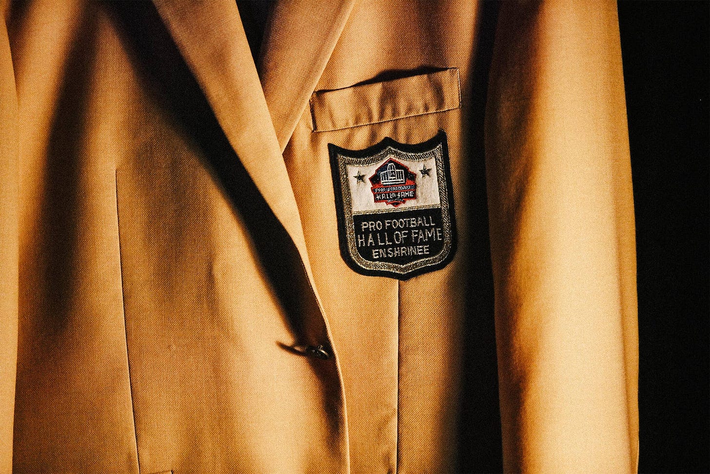 A close-up view of a Pro Football Hall of Fame gold jacket and patch. A close-up view of a Pro Football Hall of Fame gold jacket and patch.