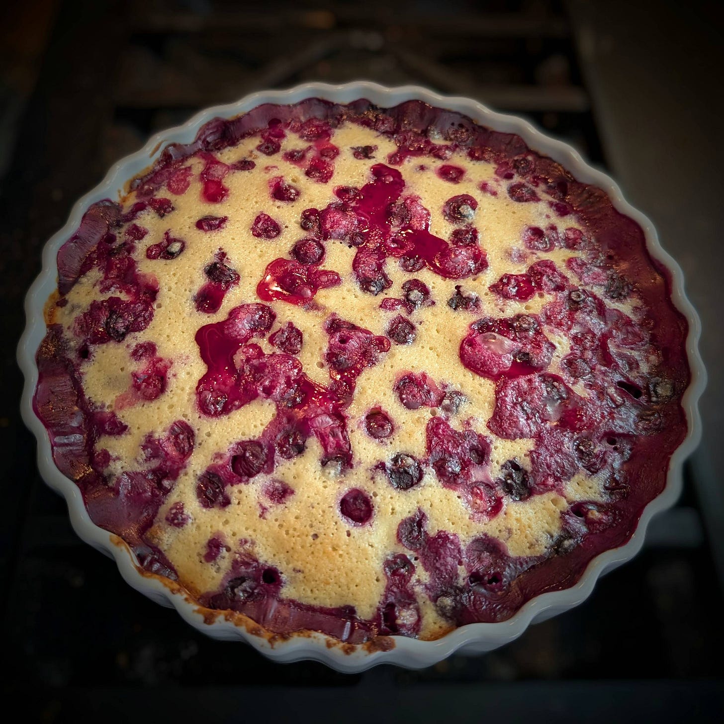 A golden tart with cooked purplish berries baked into it, in a white round dish with fluted edges