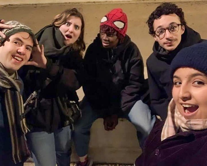 A friend group making a heart with their hands; Alex being mocked