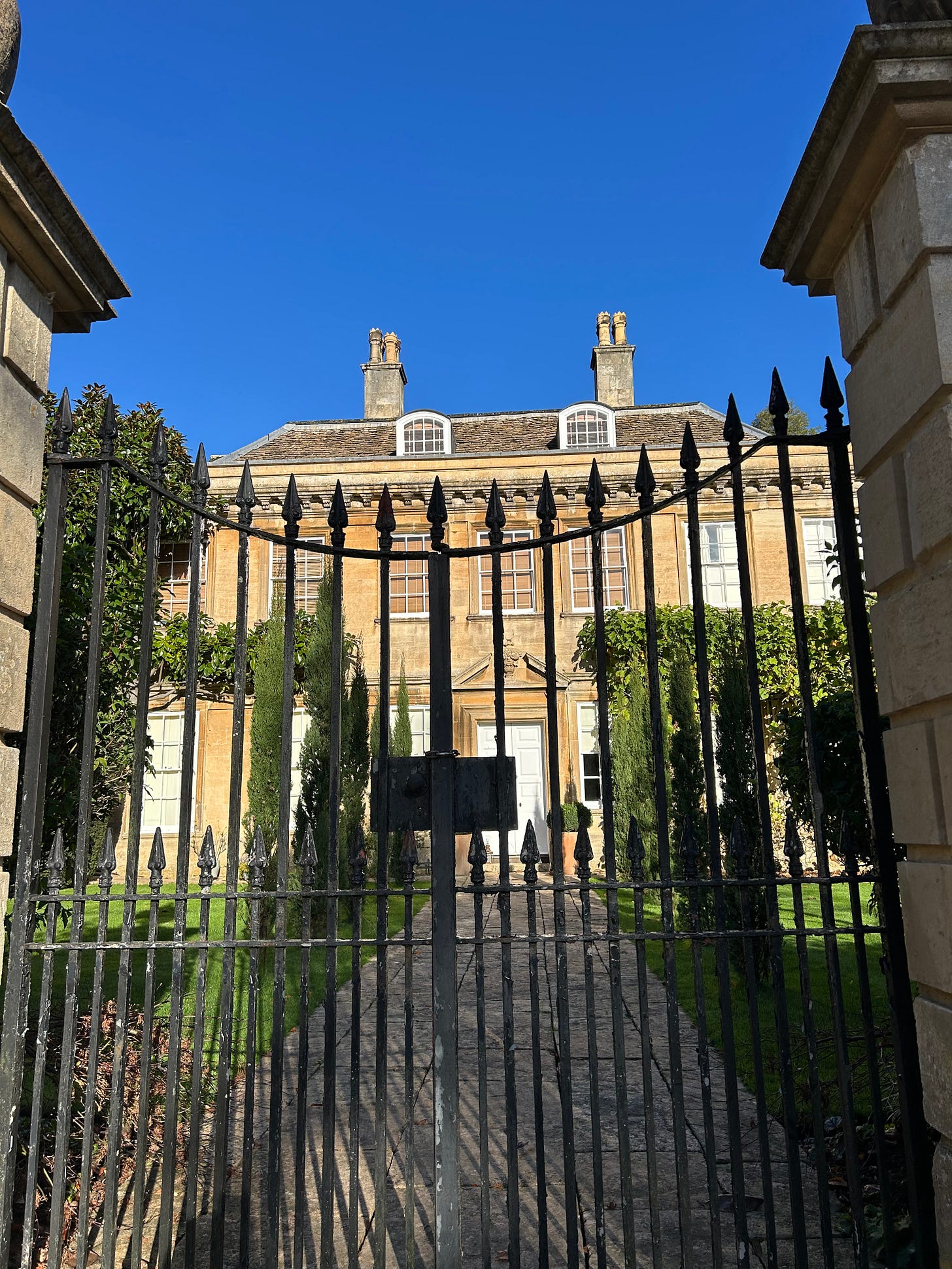 Turleigh Manor House lying behind its iron-railed gates with a pathway lined by trees under a clear blue sky. Photo: Roland Millward Turleigh Manor House lying behind its iron-railed gates with a pathway lined by trees under a clear blue sky. Photo: Roland Millward