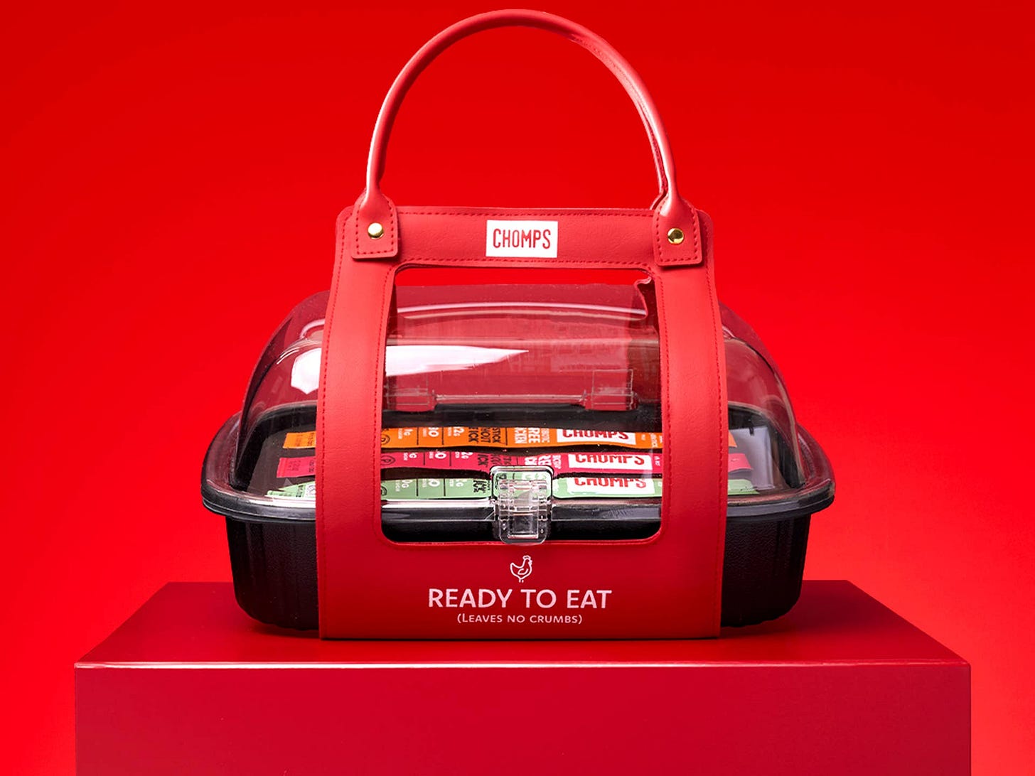 Chomps’ limited-edition “Le Chic’ken” purse inspired by a rotisserie chicken container displayed against a bright red background with chicken snack sticks inside.