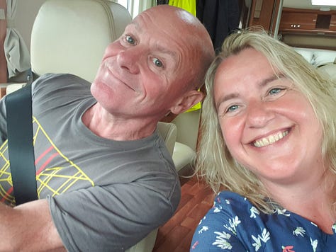 A small stove with some cooking and a Kettle, a dog lying on a bed on the dashboard of a motorhome, Dean and Jo, a cosy view of a van lit up at night, 1kg bag of teabags, motorhome and dog, champagne and glasses, Jo Scott sat at her desk