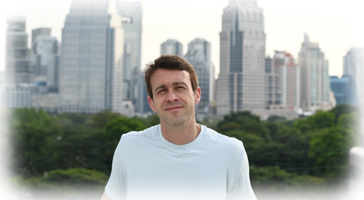 Kris, the author, standing outdoors with the Bangkok skyline and green parkland behind him.
