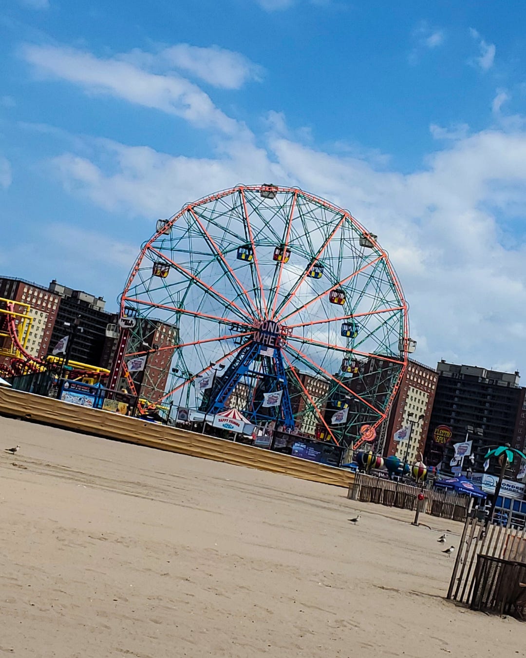 Coney Island's iconic Wonder Wheel preens proudly above the boardwalk against a white-cloud spackled blue sky..