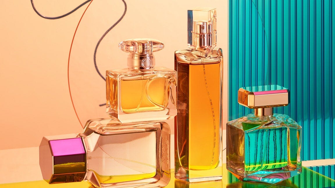 four perfume bottles stacked in front of orange and blue backdrop  best summer fragrances 2025