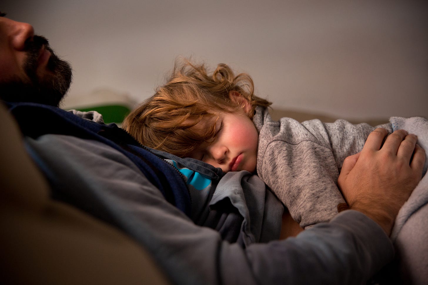 A toddler sleeps on top of a dad who is also sleeping.