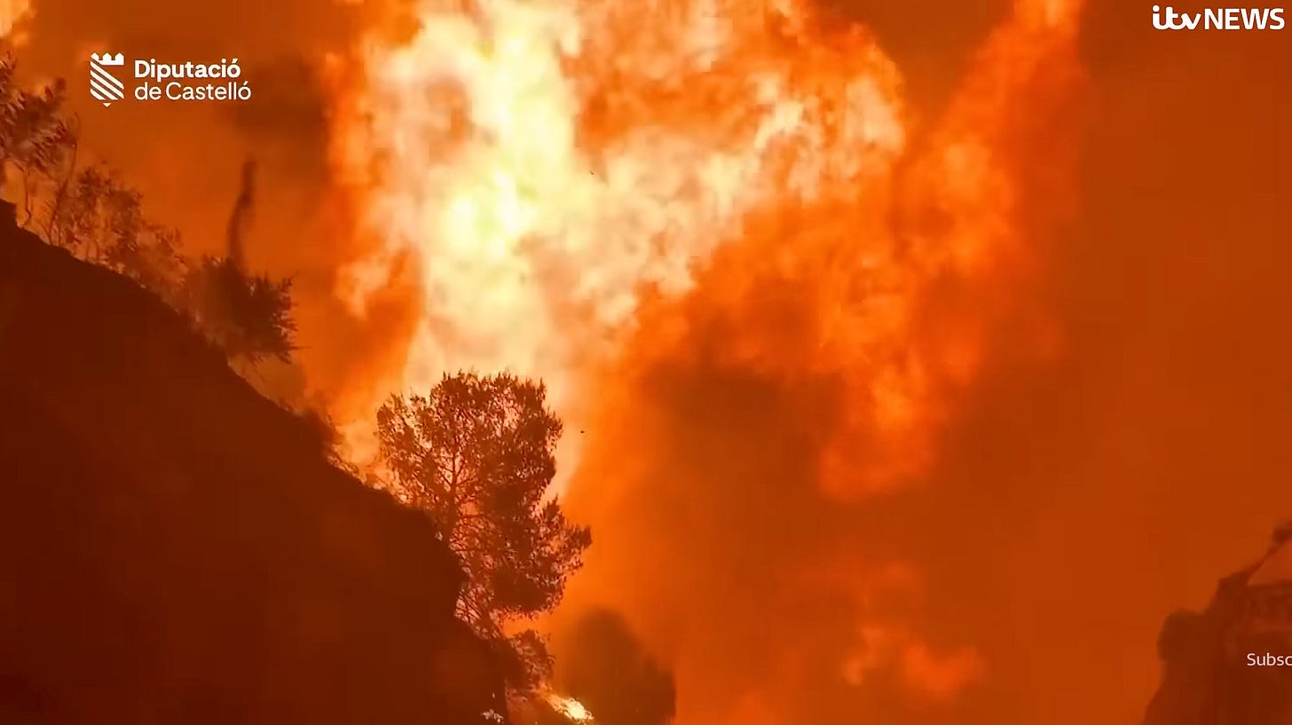 Photo looking up at hill on fire in Spain, a night time orange inferno.
