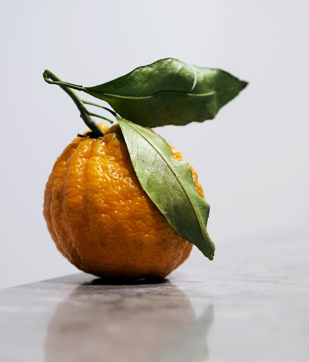 An orange with a leaf on top of it An orange with a leaf on top of it
