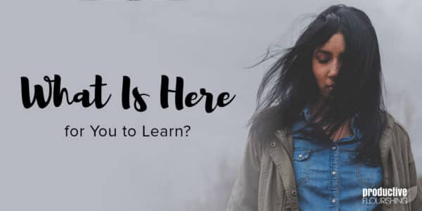 A woman looks down at the ground as her hair sweeps over her face. Text Overlay: What Is Here for You to Learn? A woman looks down at the ground as her hair sweeps over her face. Text Overlay: What Is Here for You to Learn?