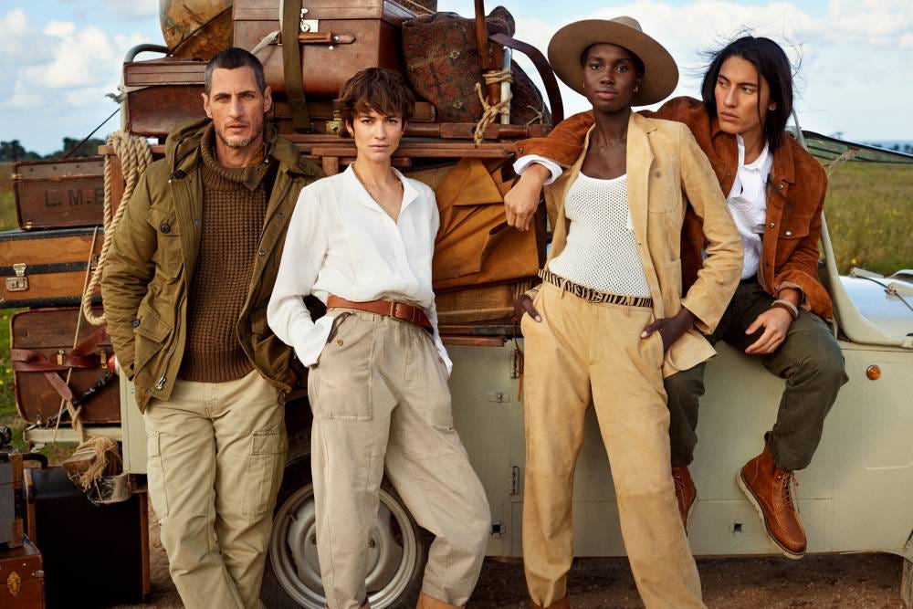 Four people of multiple races posing in front of a vehicle laden with leather travel bags