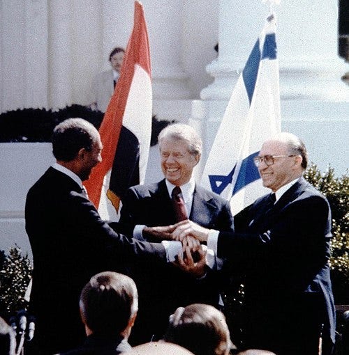 A triple handshake between Jimmy Carter and two other men, before Israeli and Egyptian flags
