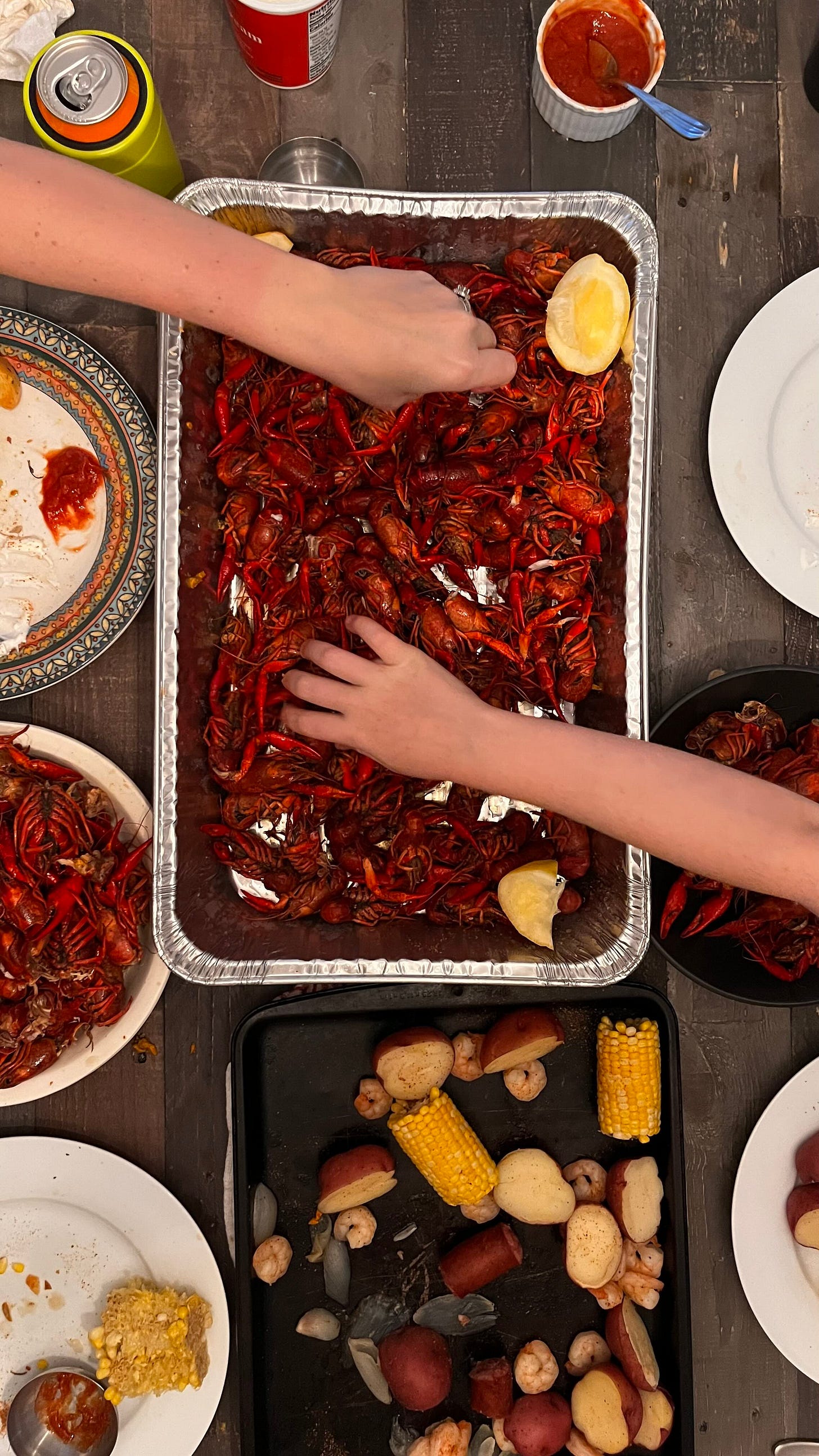 two hands digging into catfish boil on a wooden table
