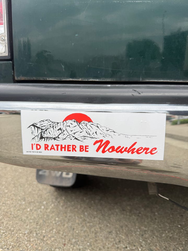 two bumper stickers on an old green truck. One says, "I'd rather be Nowhere." and the other says, "Keep Honking, I'm living my one wild and precious life."