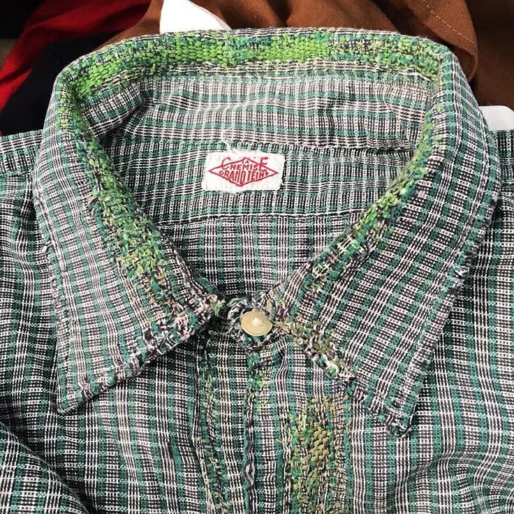 This may contain: a green and white checkered shirt sitting on top of a wooden table next to other clothing