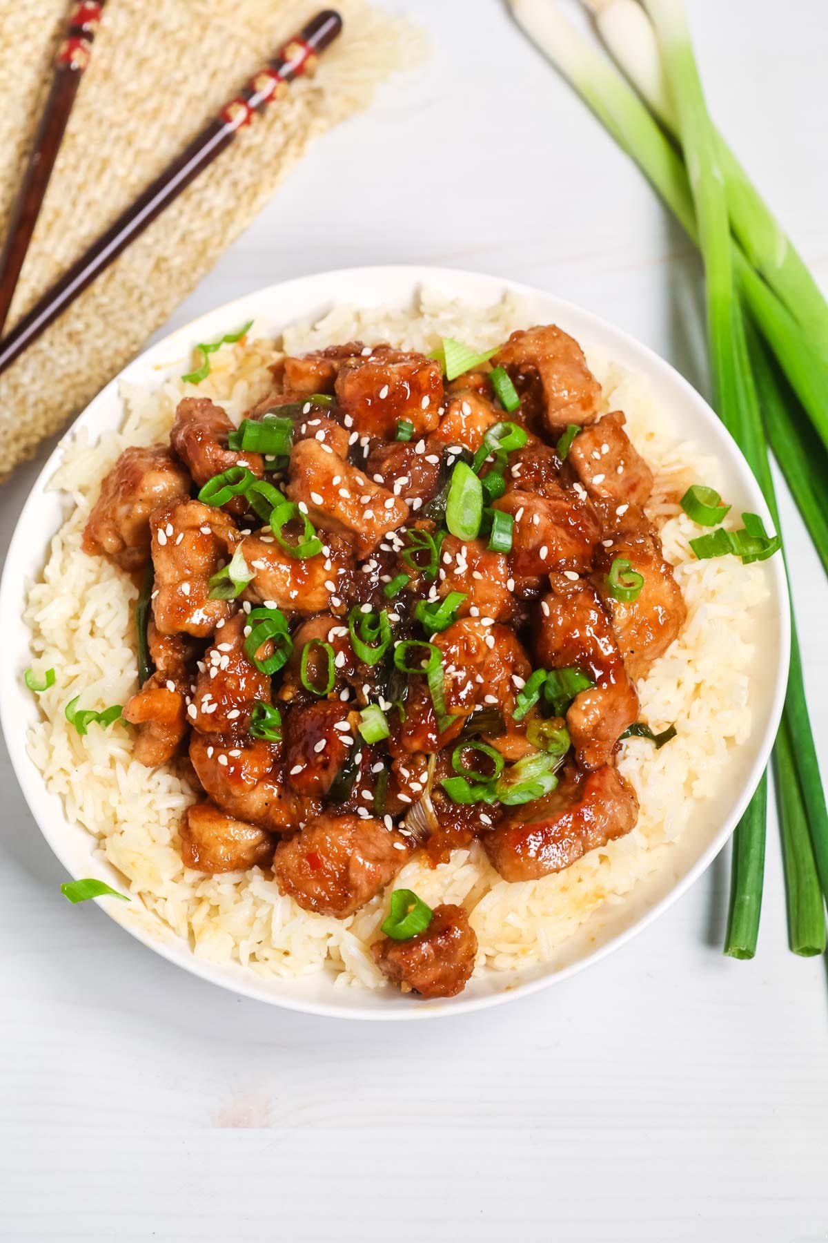 Mongolian pork atop a bowl of rice with green onions and sesame seeds on top.