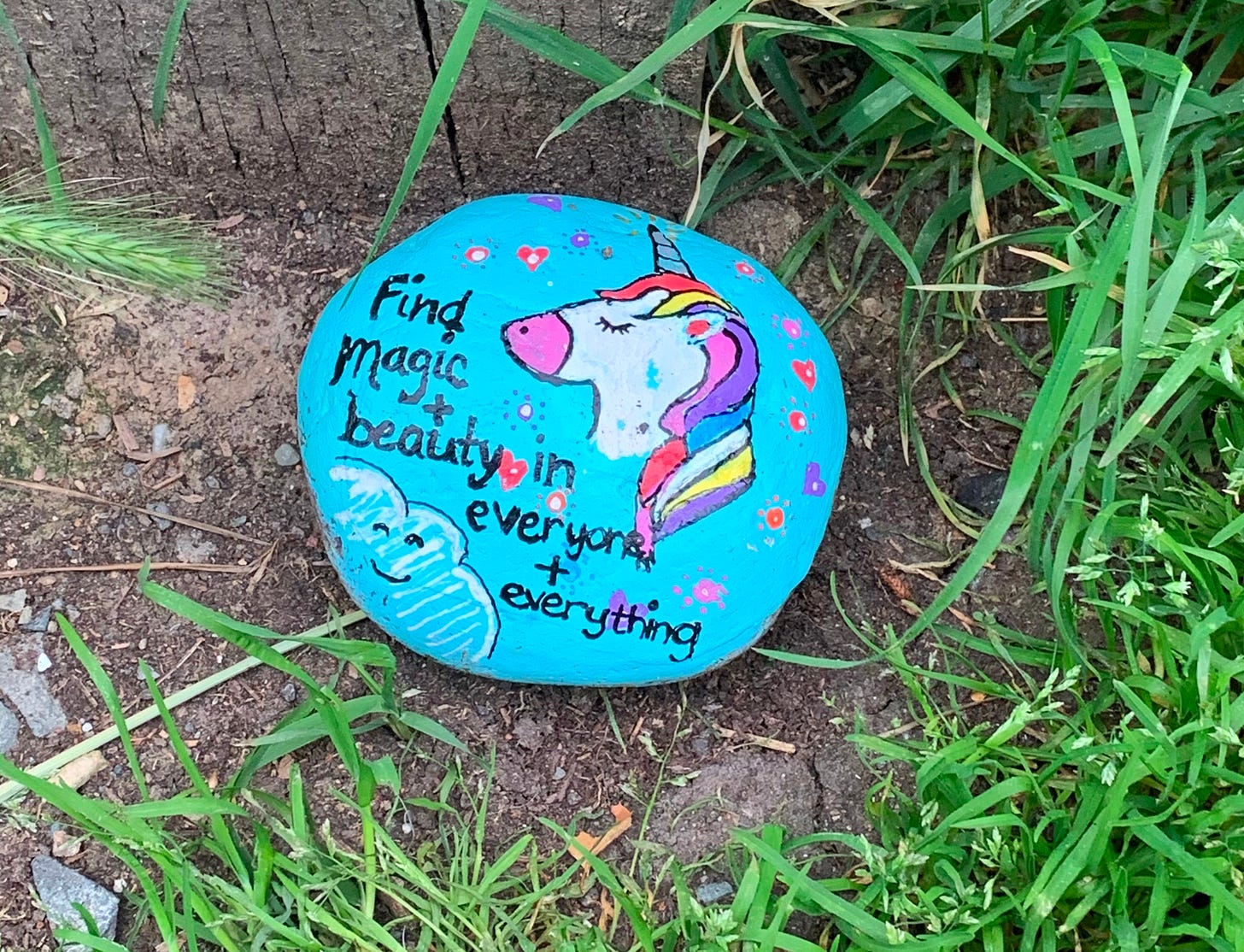 Painted rock sitting in dirt with text "Find magic and beauty in everyone and everything"