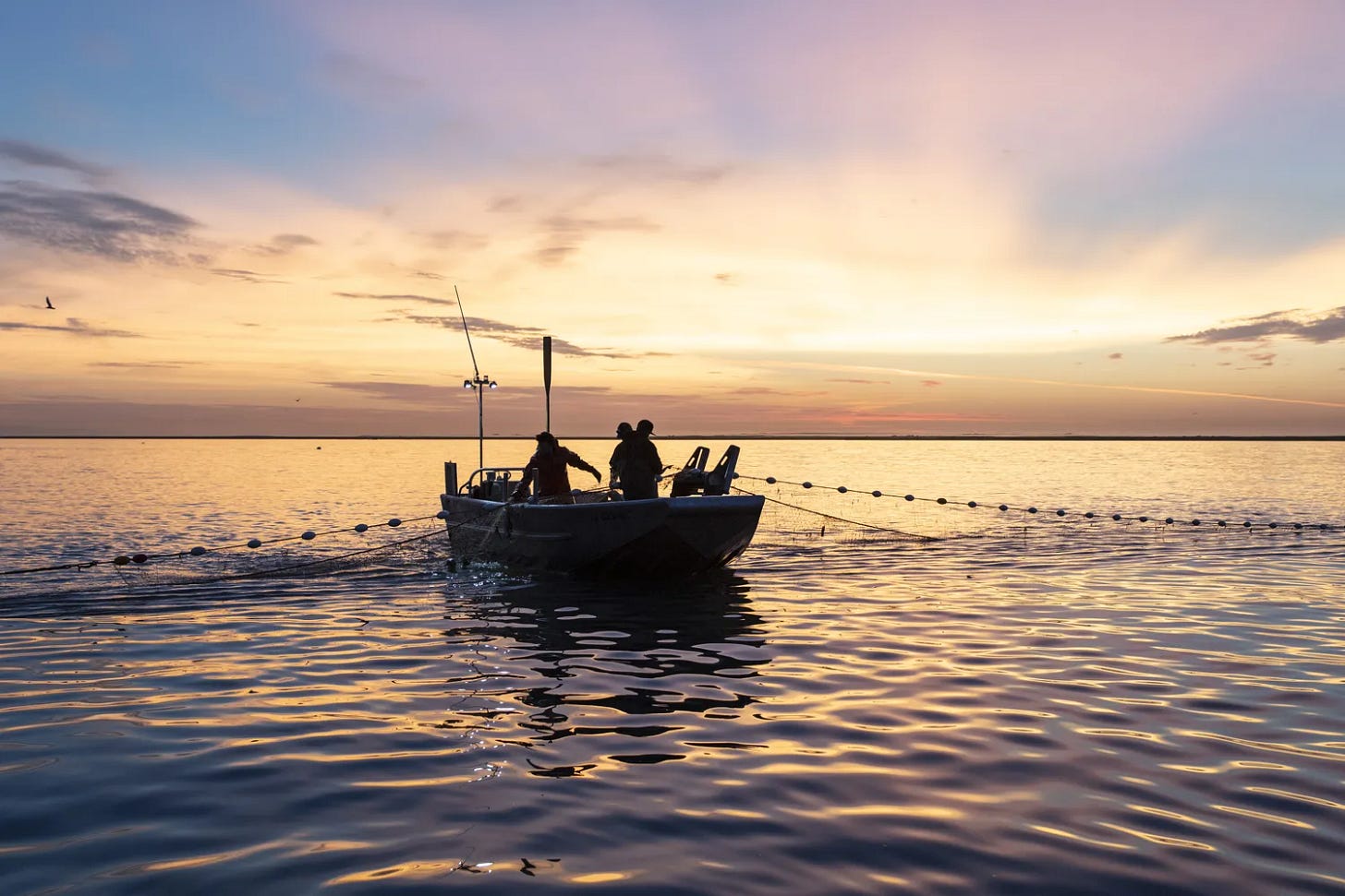 A fishing vessel on calm water at sunset, silhouetted against the light A fishing vessel on calm water at sunset, silhouetted against the light