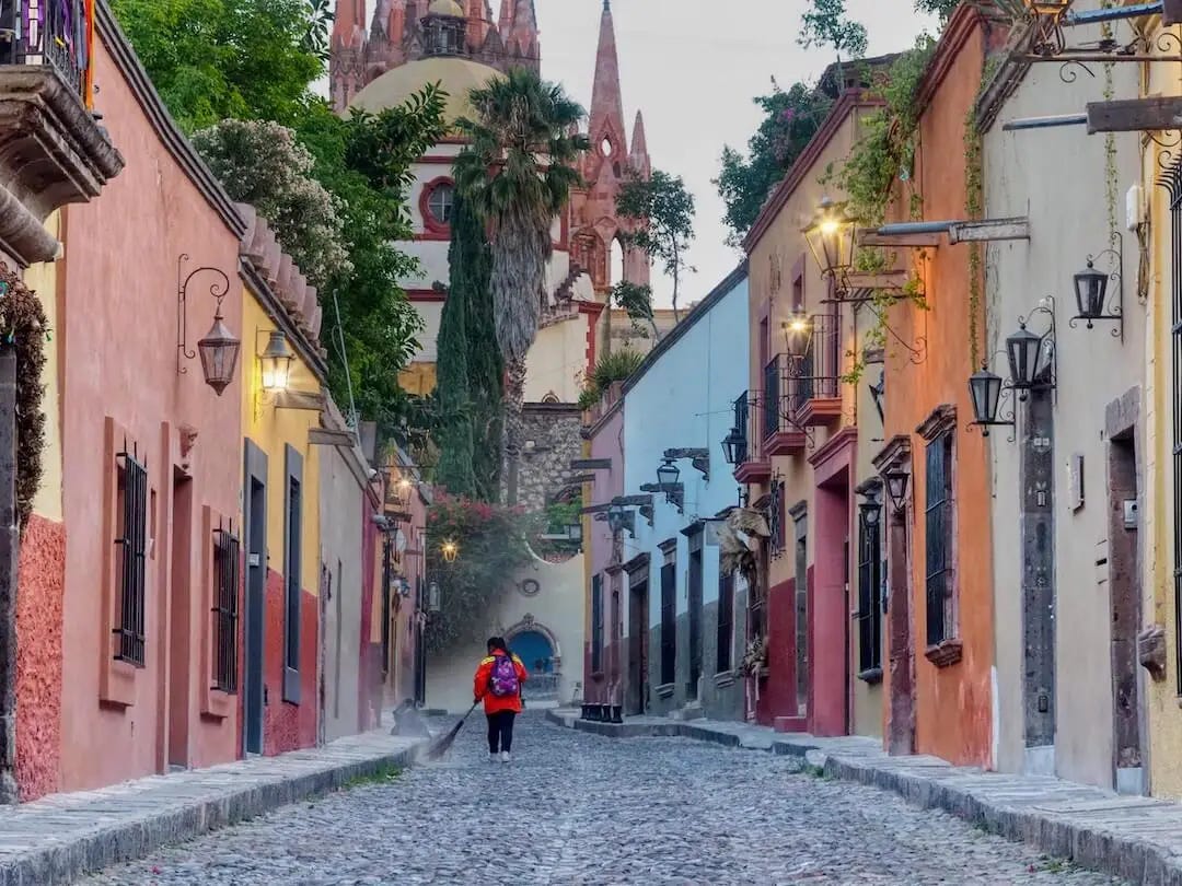 Cobblestone street with a woman sweeping and colourful buildings on either side