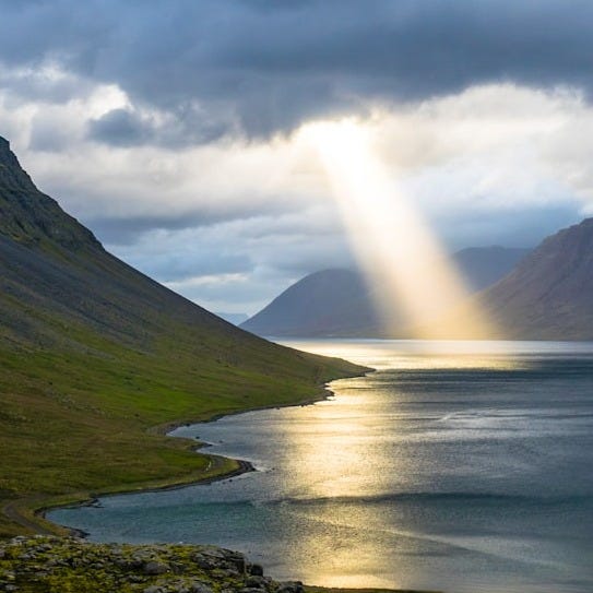 sun reflection on calm water near green mountains
